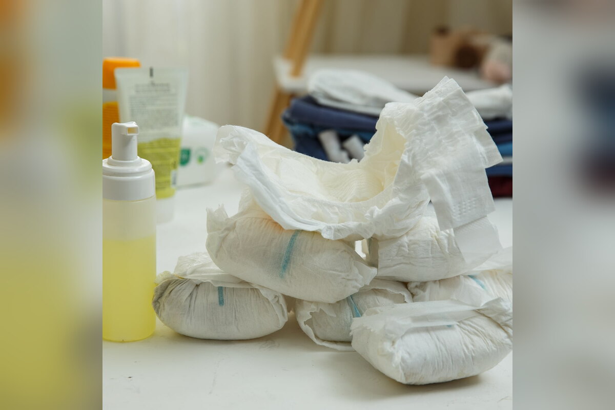 Diapers piled next to a bottle of yellow liquid used for absorbency testing