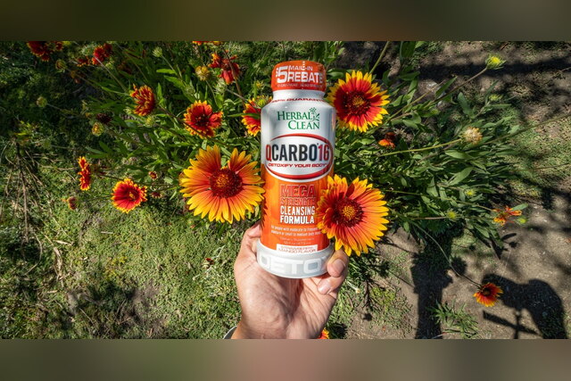 Hand holding a QCarbo16 detox drink bottle among orange flowers