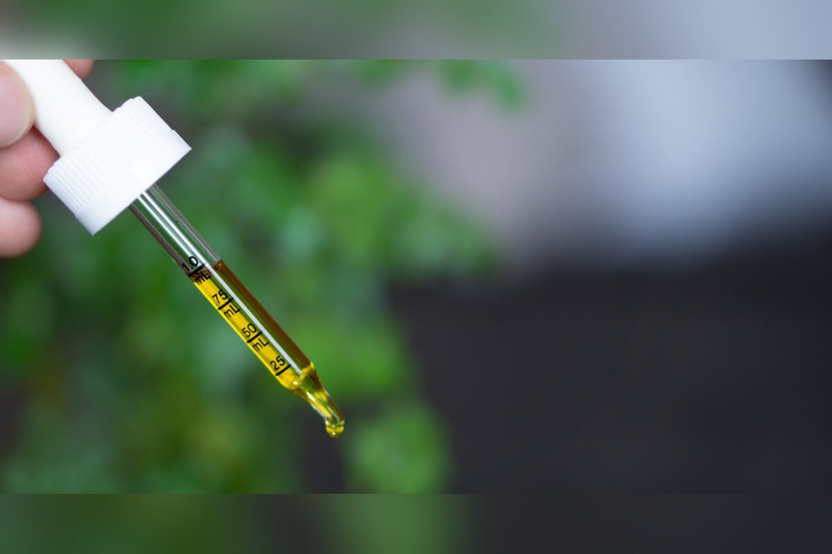Dropper releasing a drop of CBD oil beside a hemp plant