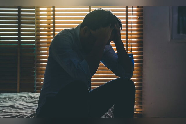 Depressed man sitting on a bed with his head in his hands