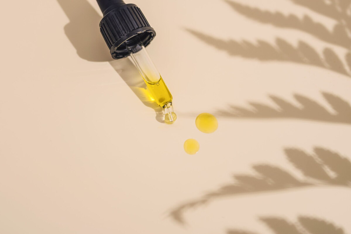Dropper releasing drops of cannabis oil on a beige background