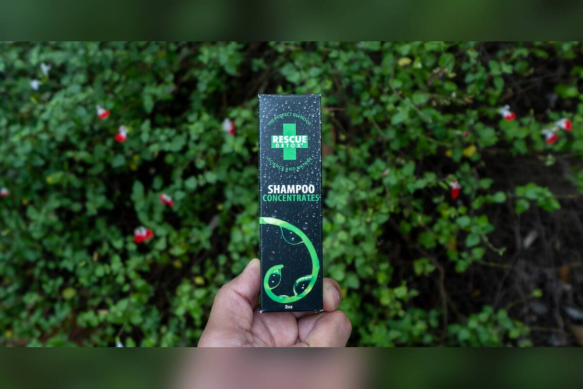 Hand holding a Rescue Detox Shampoo box in front of a green hedge
